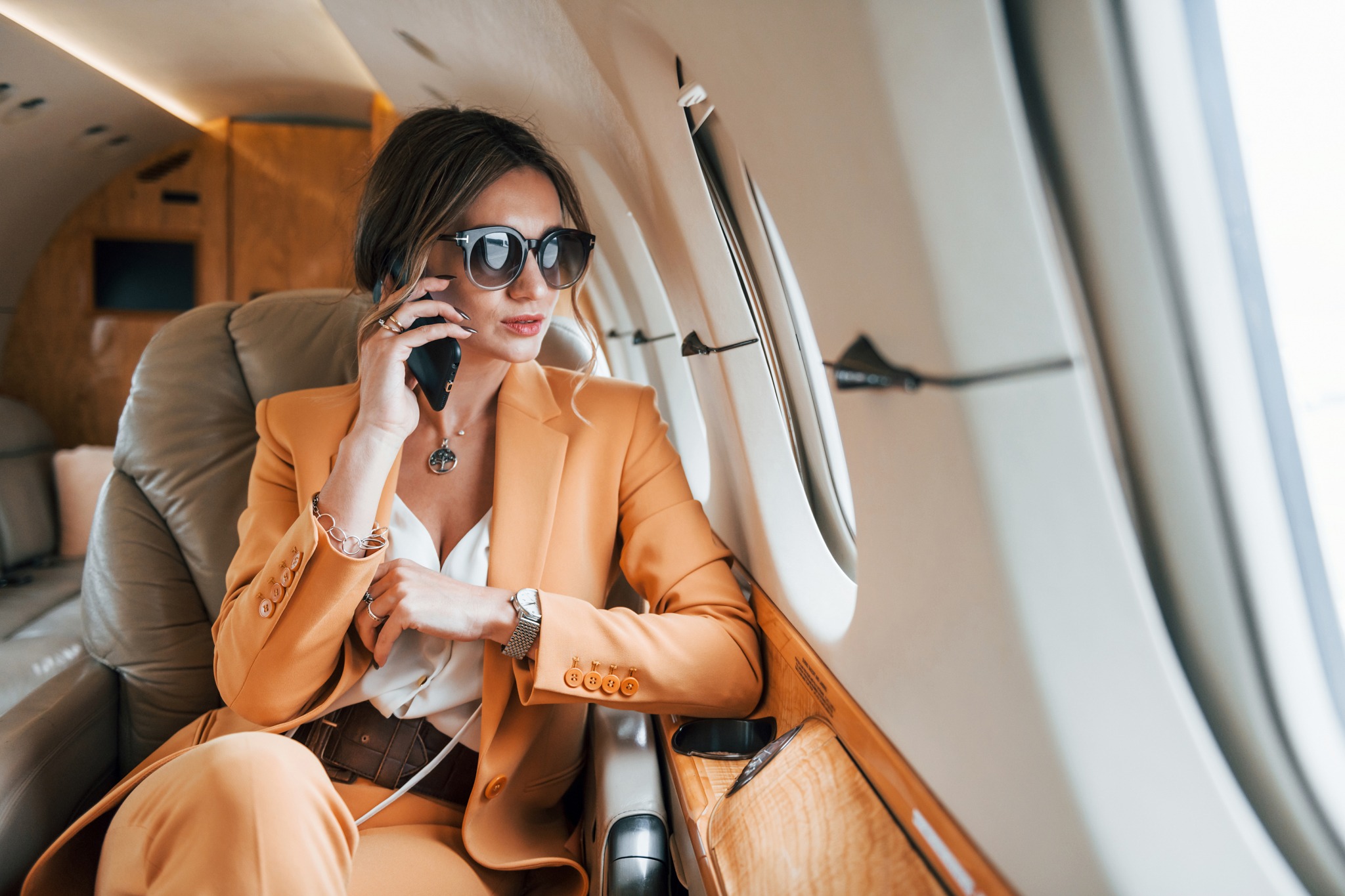 Uses phone. Young passenger woman in yellow clothes is flying in the plane